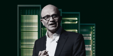 Man in a suit stands in front of a row of server racks.