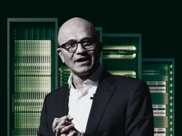 Man in a suit stands in front of a row of server racks.